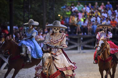 women in skull costumes riding horses